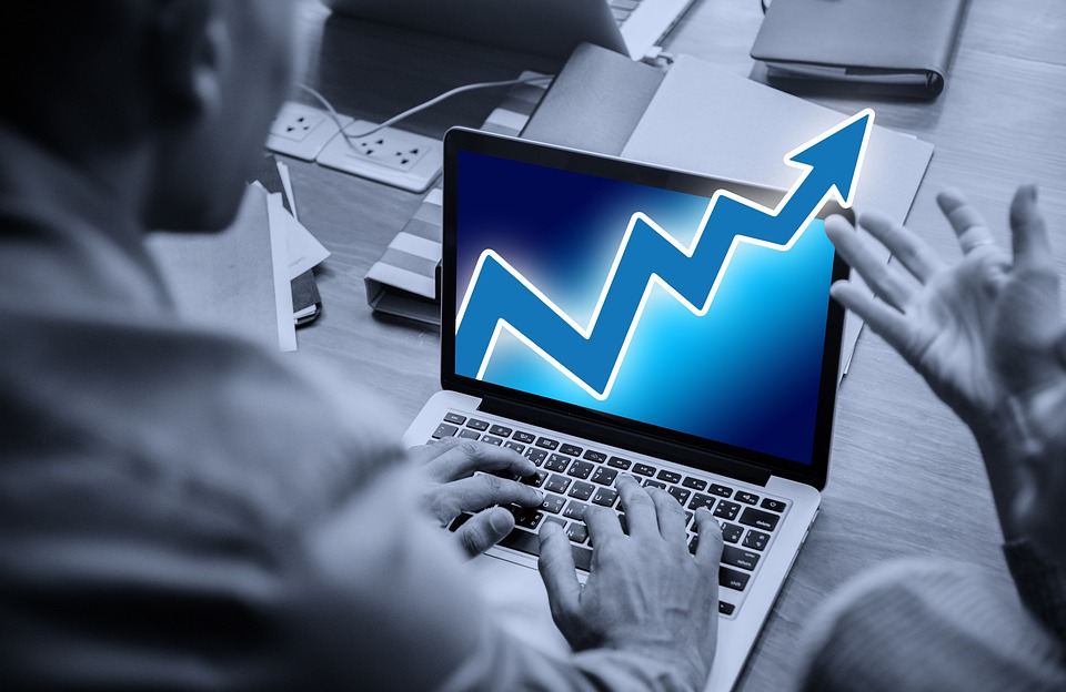 A person using a laptop displays an upward trending graph on the screen, indicating growth or success.